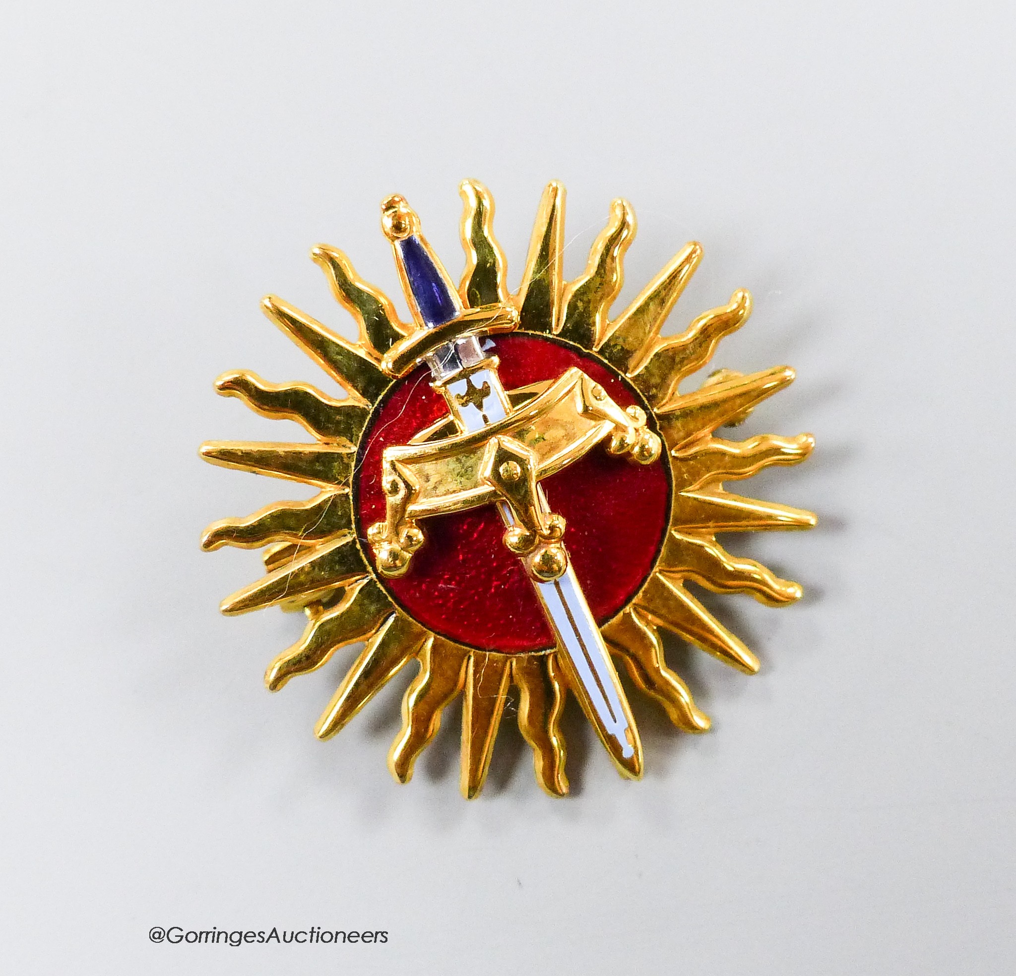A modern 9ct gold and red enamel brooch, modelled as a sword and crown, with sun background, Garrard & Co, London, 1990, 30mm, gross weight 9 grams, with Garrards box.
